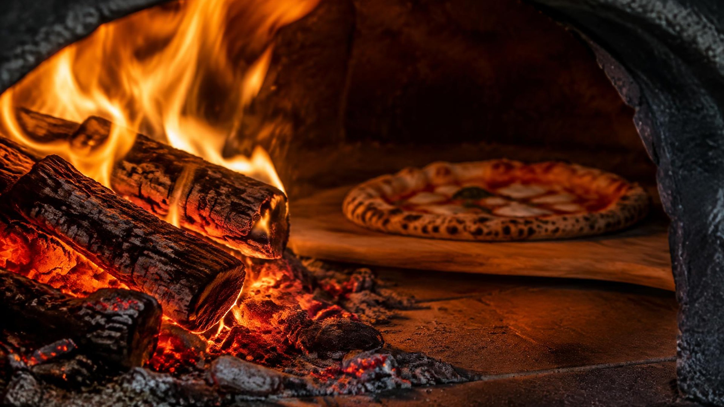 Glühende Holzscheite im Ofen und Pizza auf einem Holzschieber